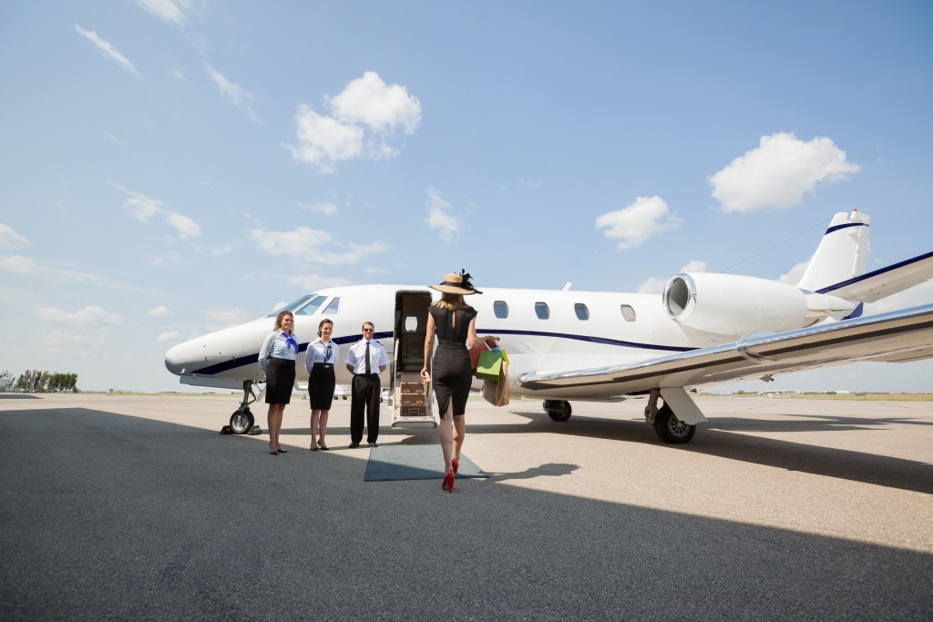 Elegant woman walking towards a private jet at the airport terminal, exuding luxury and exclusivity – The Private Yacht Club.