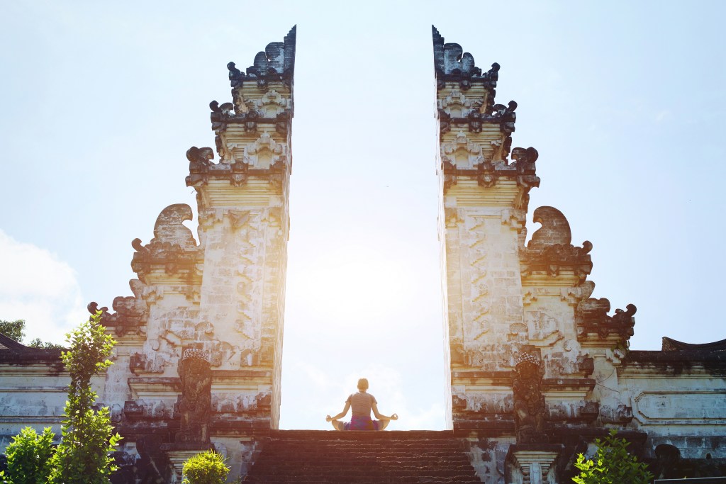 Woman practicing yoga in a serene Bali temple, meditating for spirituality and enlightenment – Wellness and Vitality – The Private Yacht Club.